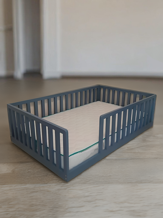 A gray floor bed with a wooden slatted base and a mattress, placed on a wooden floor against a wall.