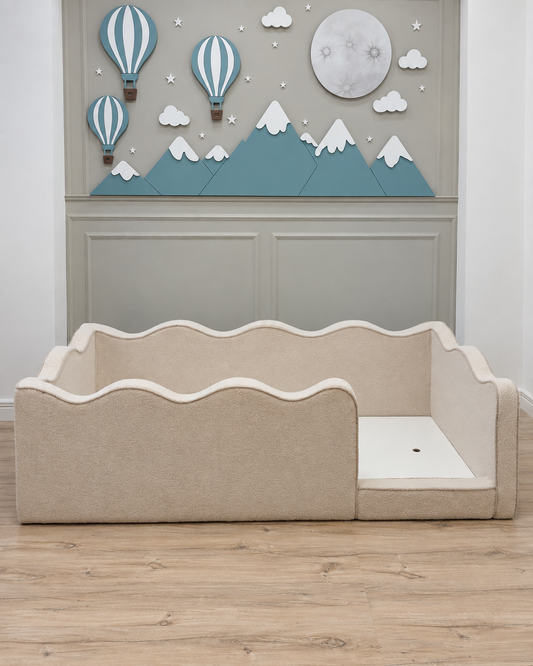A beige upholstered children's bed with a wavy scalloped headboard and side rails