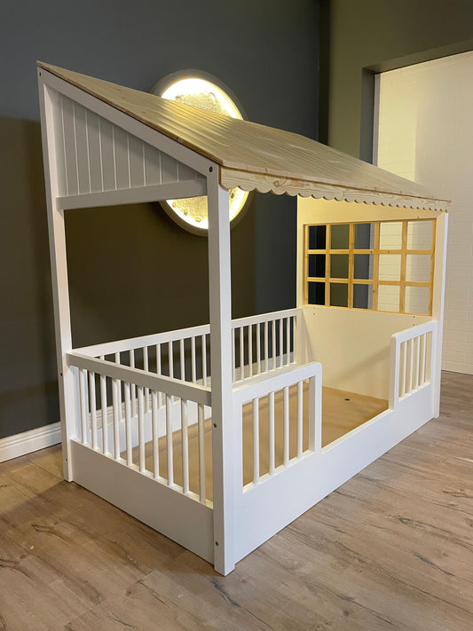 Children's playhouse with a wooden roof and white base on a wooden floor.