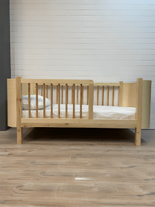 Wooden crib with mattress on a wooden floor against a light-colored wall.