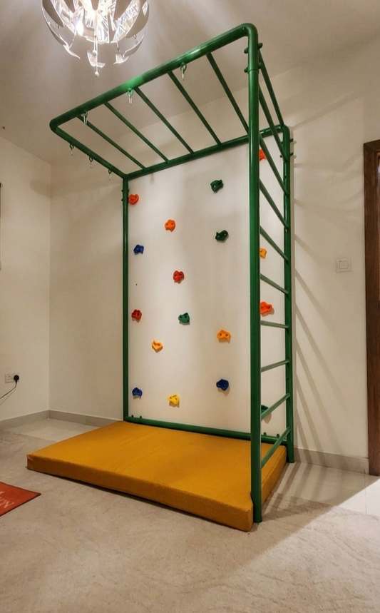 A green indoor climbing frame with a yellow padded mat base, colorful climbing rocks.