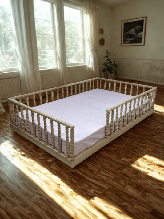 White spindle bed in a room with large windows and wooden floor.