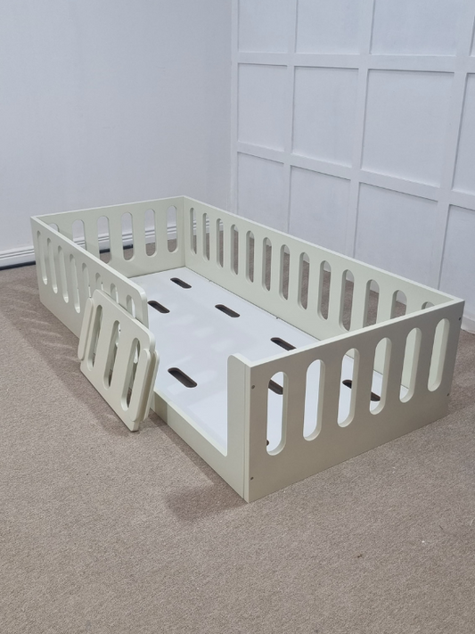 White crib with a white mattress on a gray carpeted floor.