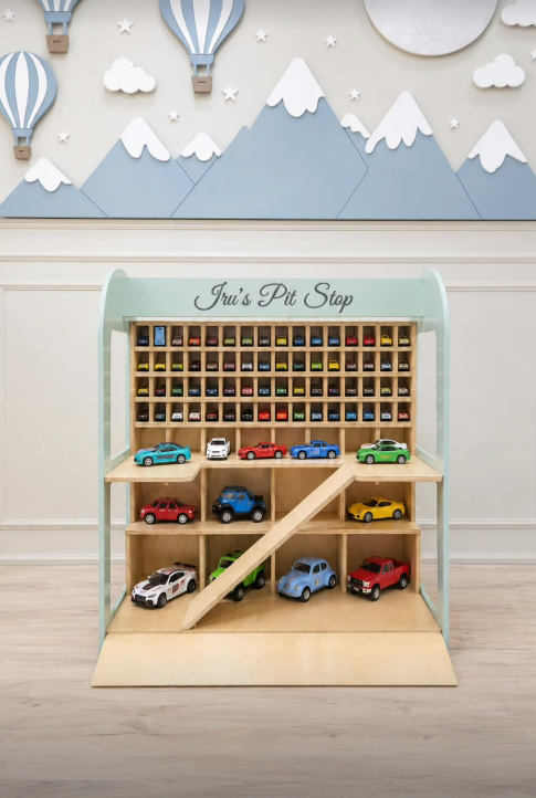 A wooden toy car garage playset labeled with a light natural wood interior, pale mint green frame, and multiple colorful toy cars arranged on shelves and ramps. 
