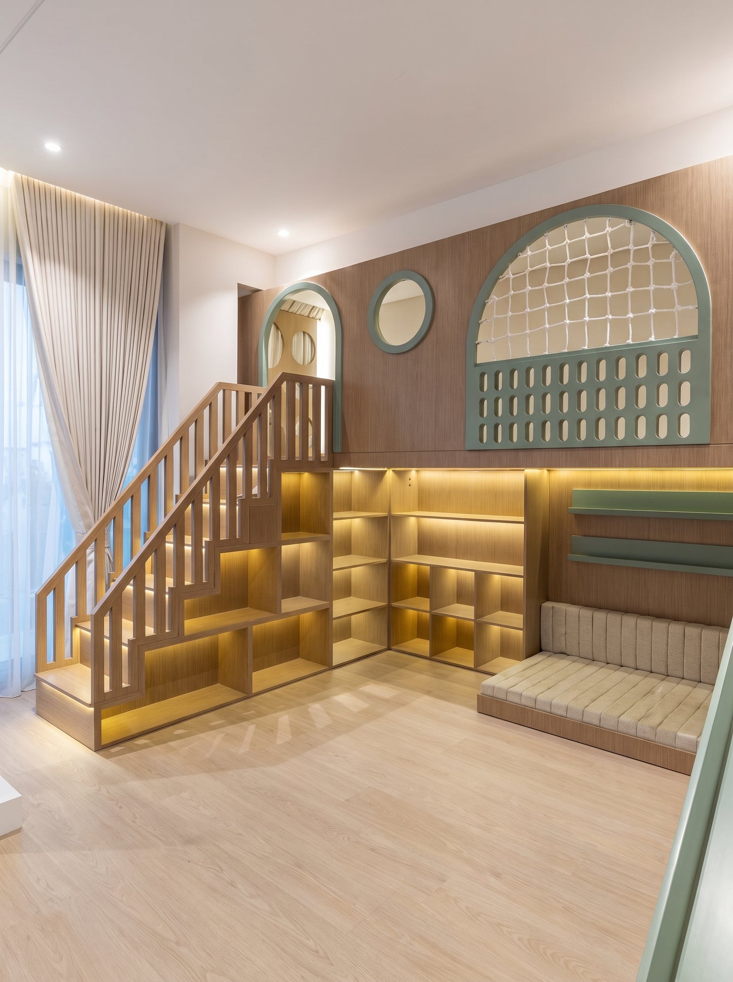 A modern wooden loft staircase with integrated shelving and warm under-step built-in LED lighting, next to a cushioned reading nook with a striped cushion and decorative arched window details.