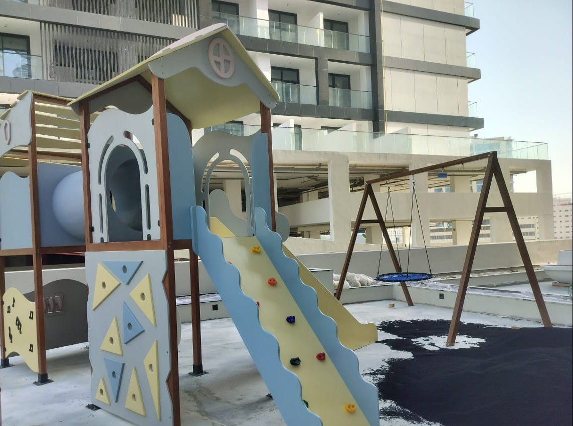 A colorful children's playground structure on a rooftop, featuring a climbing slide, a tunnel, and a swing set in the background. 