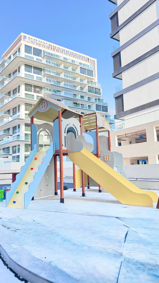 A children's playground structure with a yellow slide, blue climbing slide, and small roof play area, situated outdoors.