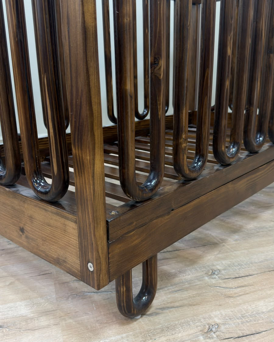 Close-up of a dark brown wooden crib or bassinet frame with curved guard rails and a slatted base.
