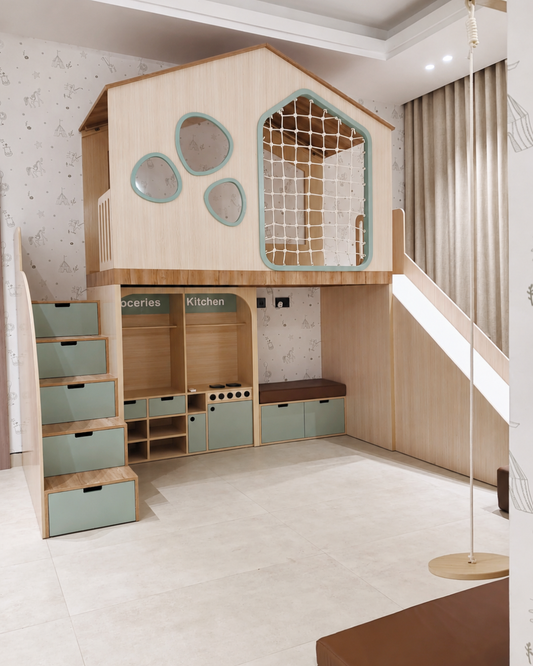 A children's loft playhouse with an elevated wooden house structure, rope frame, integrated stairs with mint green storage drawers, a play kitchen and groceries area, underneath seating, and a slide.
