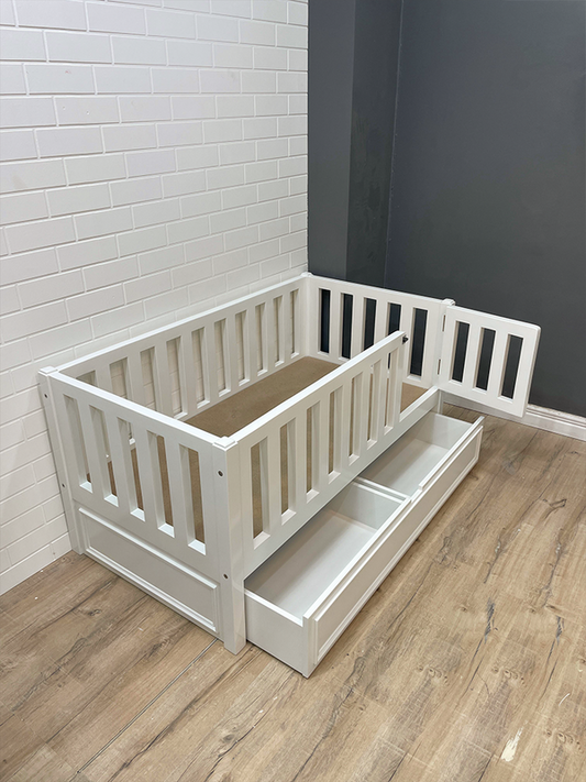 A white toddler bed with a storage drawer underneath, pictured in a room setting.